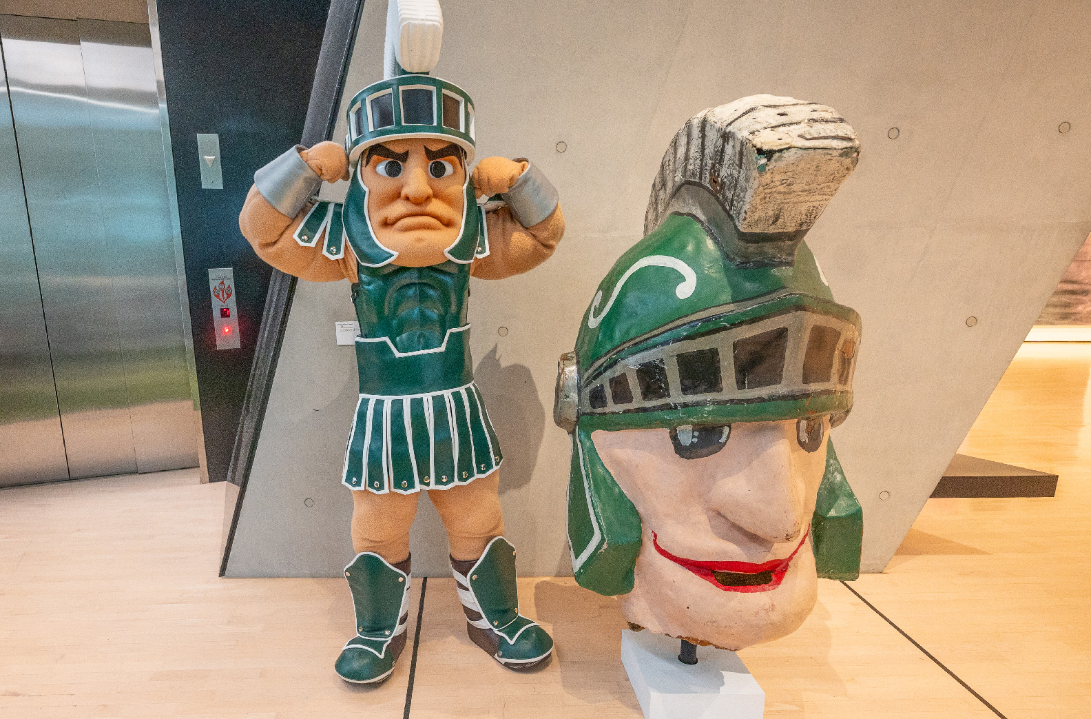 Sparty flexing muscles next to Sparty helmet 